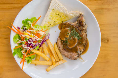 Pork chop steak with potato salad and toast on a white plateの写真素材