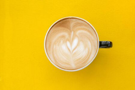 A cup of heart-shaped coffee in a red cup on a yellow wooden floor.の写真素材