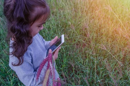 Cute Asian girl is playing on the grass phone.の写真素材