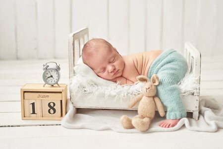 Cute newborn little boy sleeping in a white crib with toys. Baby goods packaging template. Closeup...