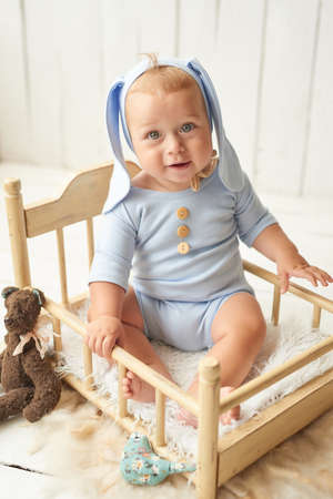 Easter Baby boy sitting on crib. Easter bunny. Children Protection Day. Happy childhood. Early child development. Educational wooden toys. Mother's day card. Child plays with toys. Happy Baby.の写真素材