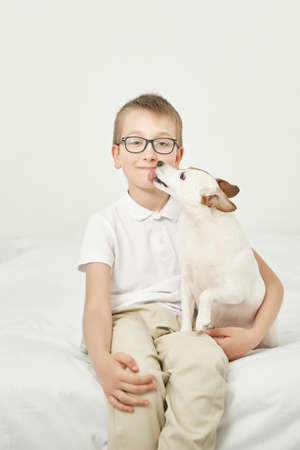 Boy on bed with dog jack russell terrier. Friendship concept. Cute little boy with funny dog on bed at home. Young Boy Hugging his Dog.の写真素材