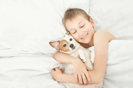 Boy on bed with dog jack russell terrier. Friendship concept. Cute little boy with funny dog on bed at home. Young Boy Hugging his Dog.の写真素材