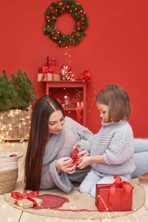 Christmas family. Red Merry Christmas tree background. Woman mother and child daughter celebrate new year. Xmas greeting card. Winter holidays and vacationsの写真素材