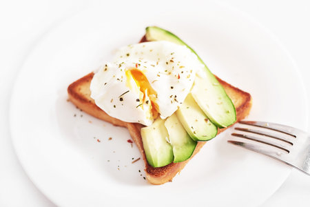 Toast with poached eggs and avocado. Healthy breakfast and food. Cozy morning. Nutrition for pregnant. Diet for women. Breakfast in hotel room or bed. Scrambled eggs sandwichの写真素材