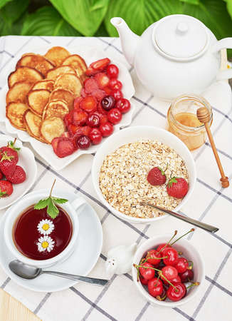 Breakfast outside. Strawberries, cherries, mini pancakes oatmeal. and honey on table. Summer picnic. Good morning conceptの写真素材