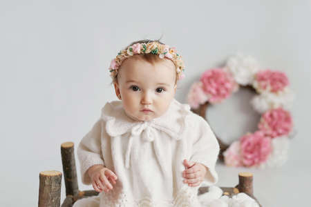 Cute baby girl in knitted clothes and wreath with teddy bear toy. Spring background with flowers....