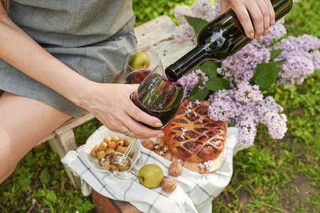 Summer picnic in the garden. Wine, pie, fruits and flowers. still life. Easter lunch and table. Woman's hands pouring glass of wine.の写真素材