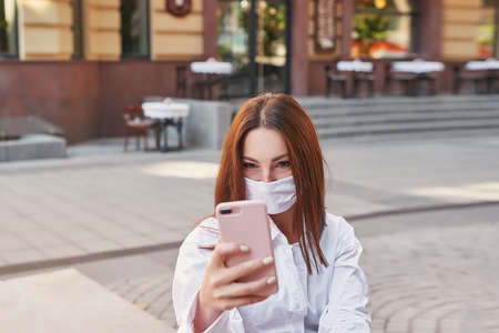 Portrait of girl on street with phone and mask. Quarantine, pandemic, self-isolation, covid.の写真素材