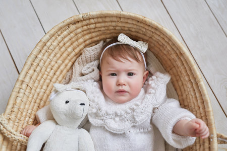 Baby girl in flower hat in wicker basket with wooden rattle. Postcard Mother's Day and Easter. Children Protection Day. World Happiness Day. Smiling child.の写真素材