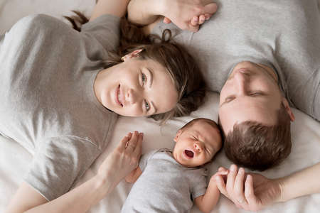 Newborn baby in mother's and father's arms on bed. Postcard Mother's and father's day. Children...