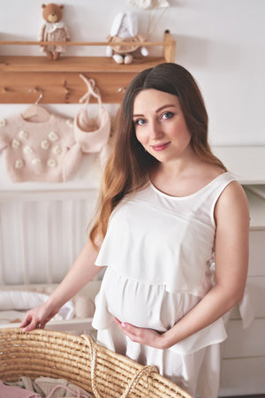 Portrait of a beautiful pregnant woman in white dress at home.