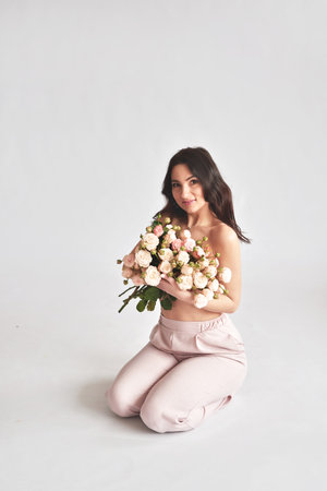 Beautiful brunette girl in pink pants with a bouquet of flowersの写真素材