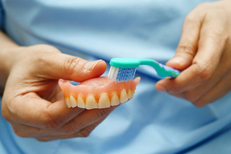 Asian senior woman patient clean teeth denture with toothbrush for chew food.