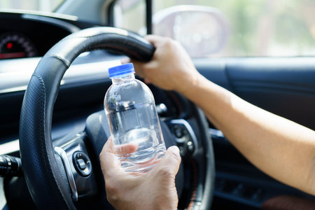 Asian woman driver holding water bottle in car.の写真素材
