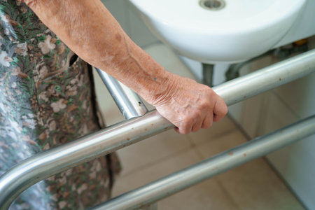Asian elderly woman patient use toilet support rail in bathroom.