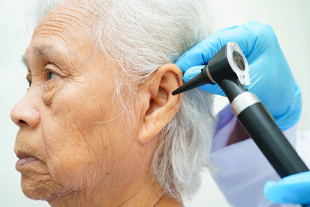 Otolaryngologist or ENT physician doctor examining senior patient ear with otoscope, hearing loss problem.の写真素材