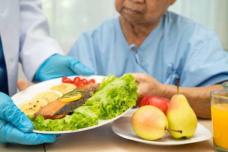 Asian elderly woman patient eating fish and vegetable salad for healthy food in hospital.の写真素材