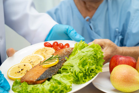 Asian elderly woman patient eating salmon stake and vegetable salad for healthy food in hospital.の写真素材