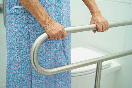 Asian elderly woman patient use toilet support rail in bathroom.