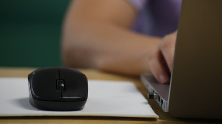 Click black computer mouse on a work desk. Working with a PC or laptop at workplace, close-up