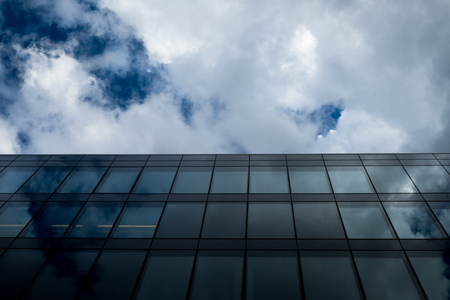 Commercial modern glass office building against cloudy sky in perspective