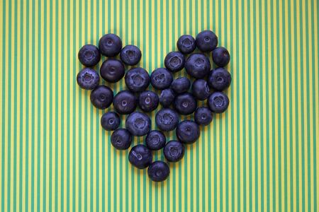 Many fresh blueberries arranged in the shape of heart on green-yellow stripe backgroundの写真素材