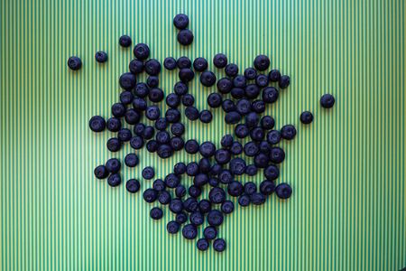 Many blueberries arranged irregularly on the green and yellow stripe background