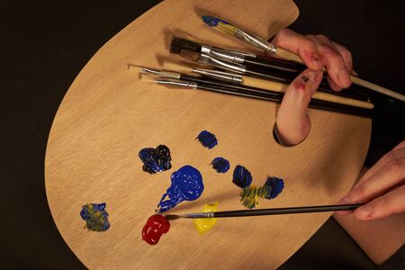 Hand holding brush with palette, paints and many brushesの写真素材