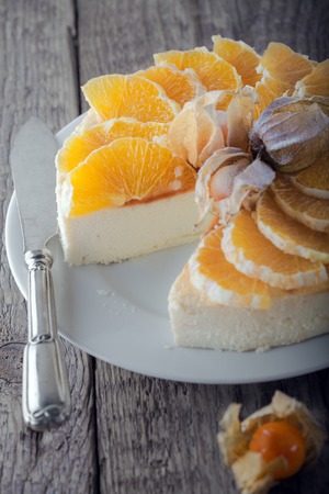 Cheesecake decorated with oranges and physalis on a plate.の写真素材