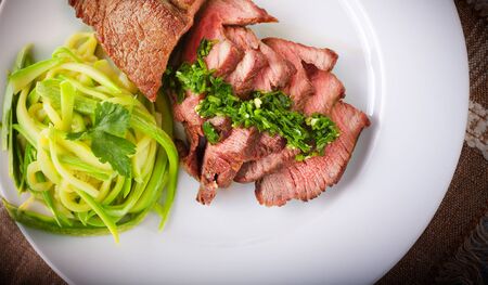 Zucchini pasta and meat on a white plateの写真素材