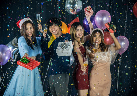 Happy group of friends celebrating Christmas and New Year Party, holding gifts and glasses of champagne looking at the camera while having Confetti sprinkles all over, selective focusの写真素材