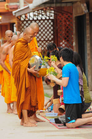 Chiang Khan, THAILAND - July 17: An unidentified men Gives food and flower offerings to a Buddhist monk on July 17, 2011 in Chiang Khan, Loei province, Thailand. Thai traditional, people will make merit making by give food to monkのeditorial素材