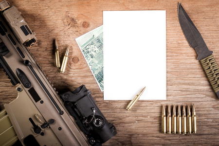 Assault rifle with bullets, paper and knife on a wooden tableの写真素材