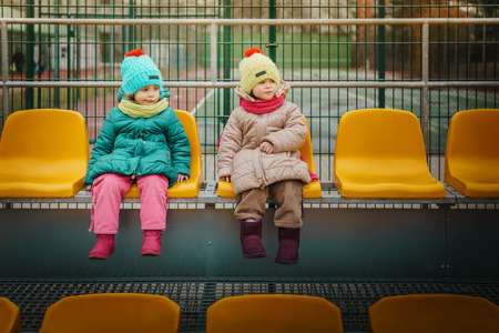 Two girls sit on the grandstand and watch football matchの写真素材