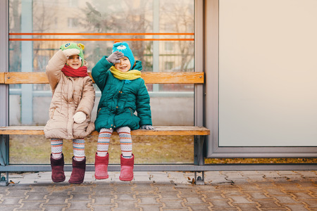 two little girls are sitting at the bus stop in the springの写真素材