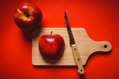 Red fresh apples chopped up on the old board on a red backgroundの写真素材