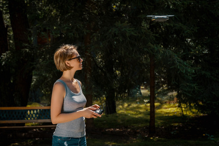 Young woman holding radio controller and flying a drone in a forest