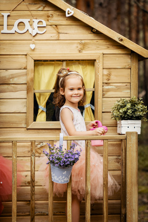 One lovely girl play with watering can in a tree house in a summer forestの写真素材
