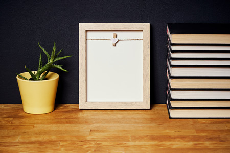 empty frame on a bright wooden shelf with a plant and books on a black wallの写真素材