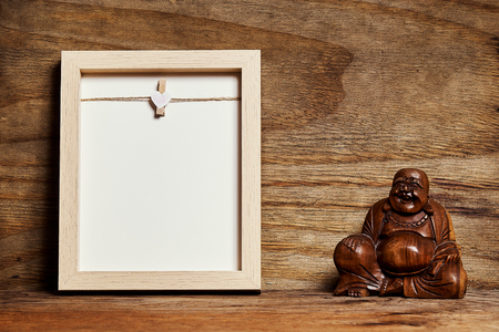 empty frame on a bright wooden shelf with a buddha on a plywood wallの写真素材