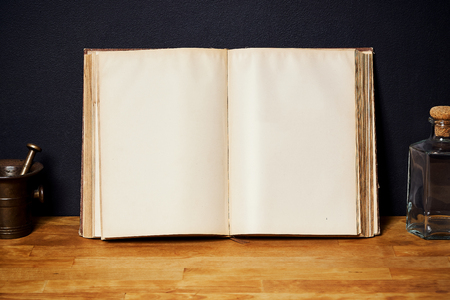 Open book on a bright wooden shelf on a black wall with a bottle and a mortarの写真素材