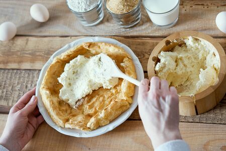 woman puts a cream on the cake on an old wooden table