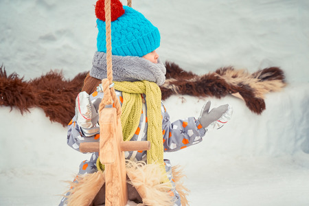 little girl is playing on a wooden carousel in winterの写真素材