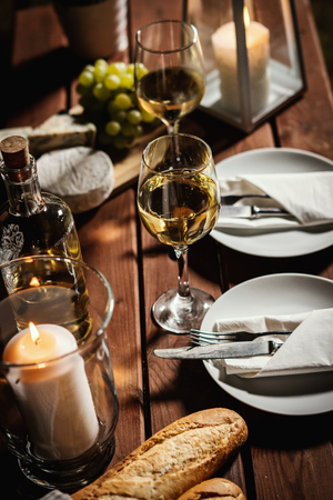 romantic dinner with two glasses of wine, a baguette and snacks on an old wooden table on a summer eveningの写真素材