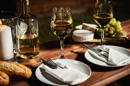 romantic dinner with a glass of wine, a baguette and snacks on an old wooden table on a summer eveningの写真素材