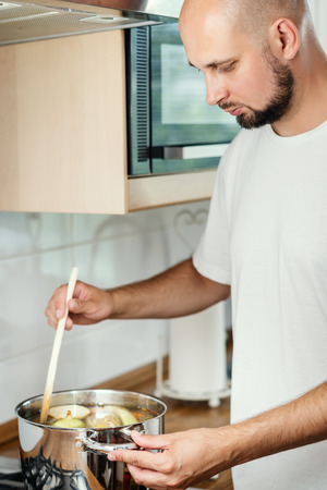 man mixes the delicious and fragrant broth in a pot on the gas stove in the kitchenの写真素材