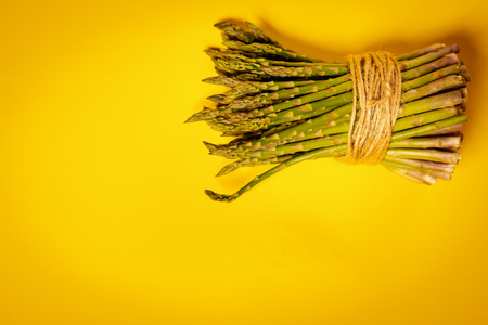 fresh green asparagus tied with a thin string on a yellow summer backgroundの写真素材