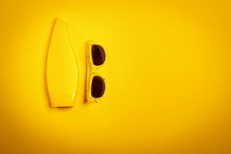 minimalistic yellow holiday background with sunglasses and sun creamの写真素材
