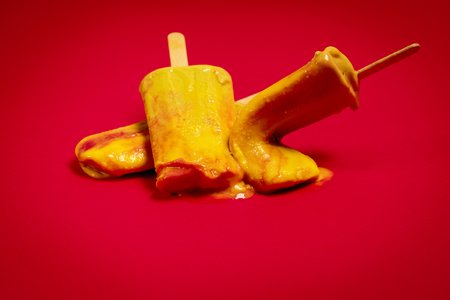 isolated and wasted delicious yellow-red ice cream on a red backgroundの写真素材